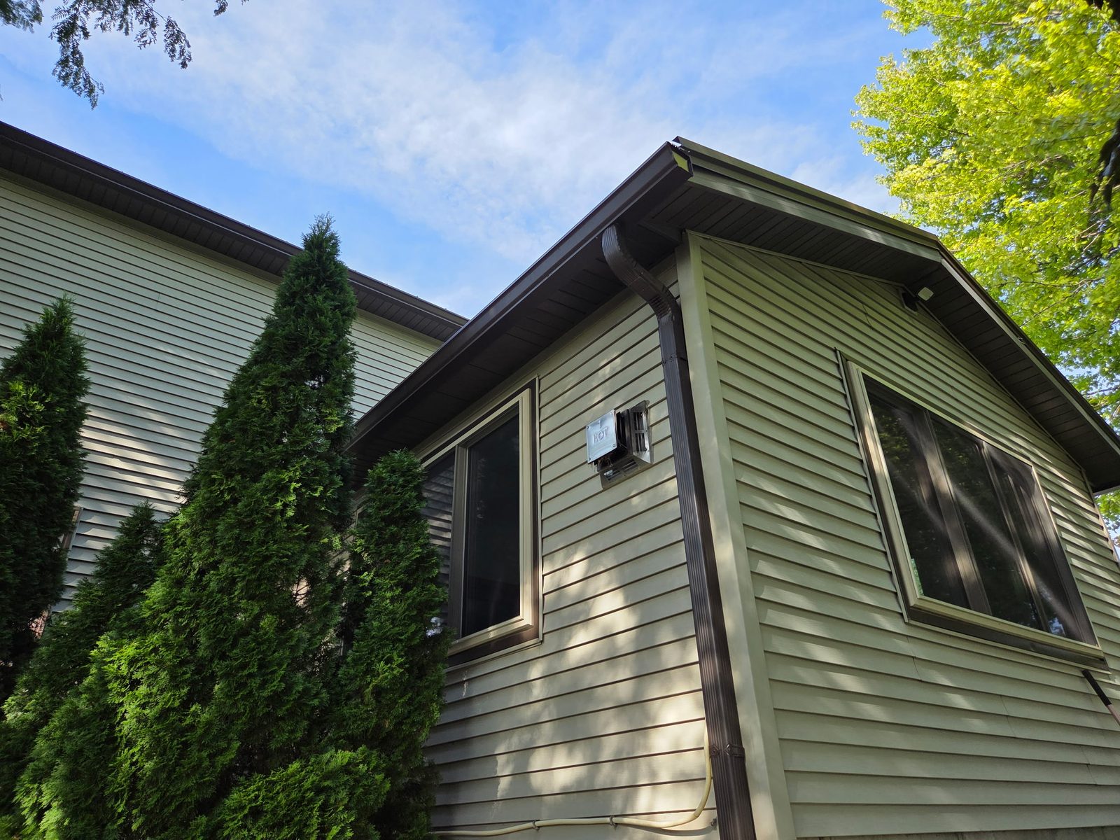 New brown seamless gutters and a corner downspout against tan siding