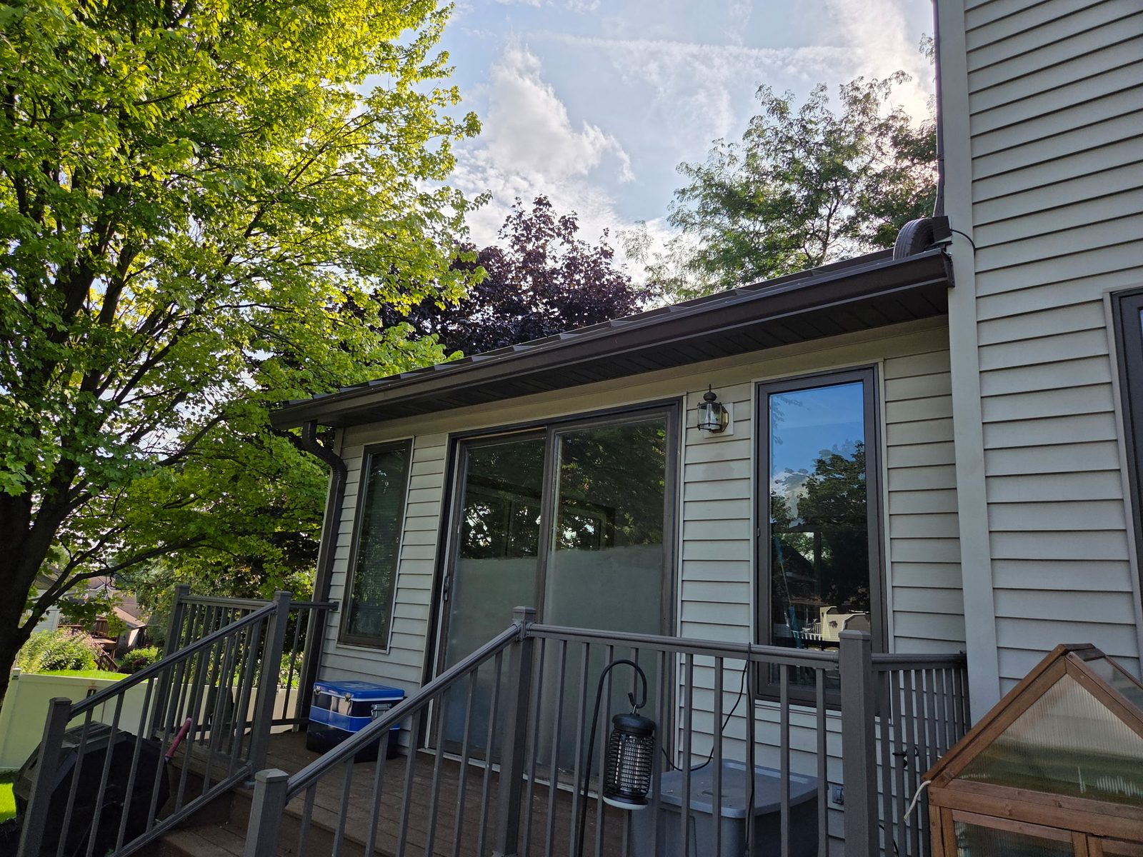 Guarded low-slope roofline over a backyard deck with new gutters and downspout