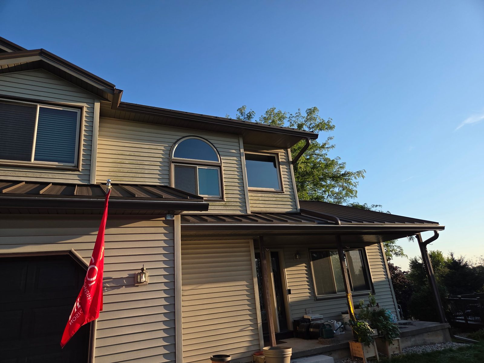Golden hour on a finished system: new seamless gutters, downspouts, and metal porch roofs on a two-story home