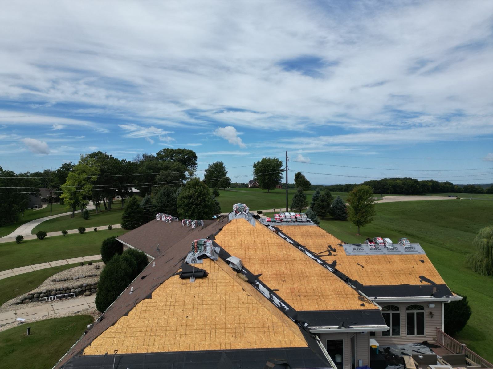Drone view: bare roof decking with new shingle bundles staged along the ridge