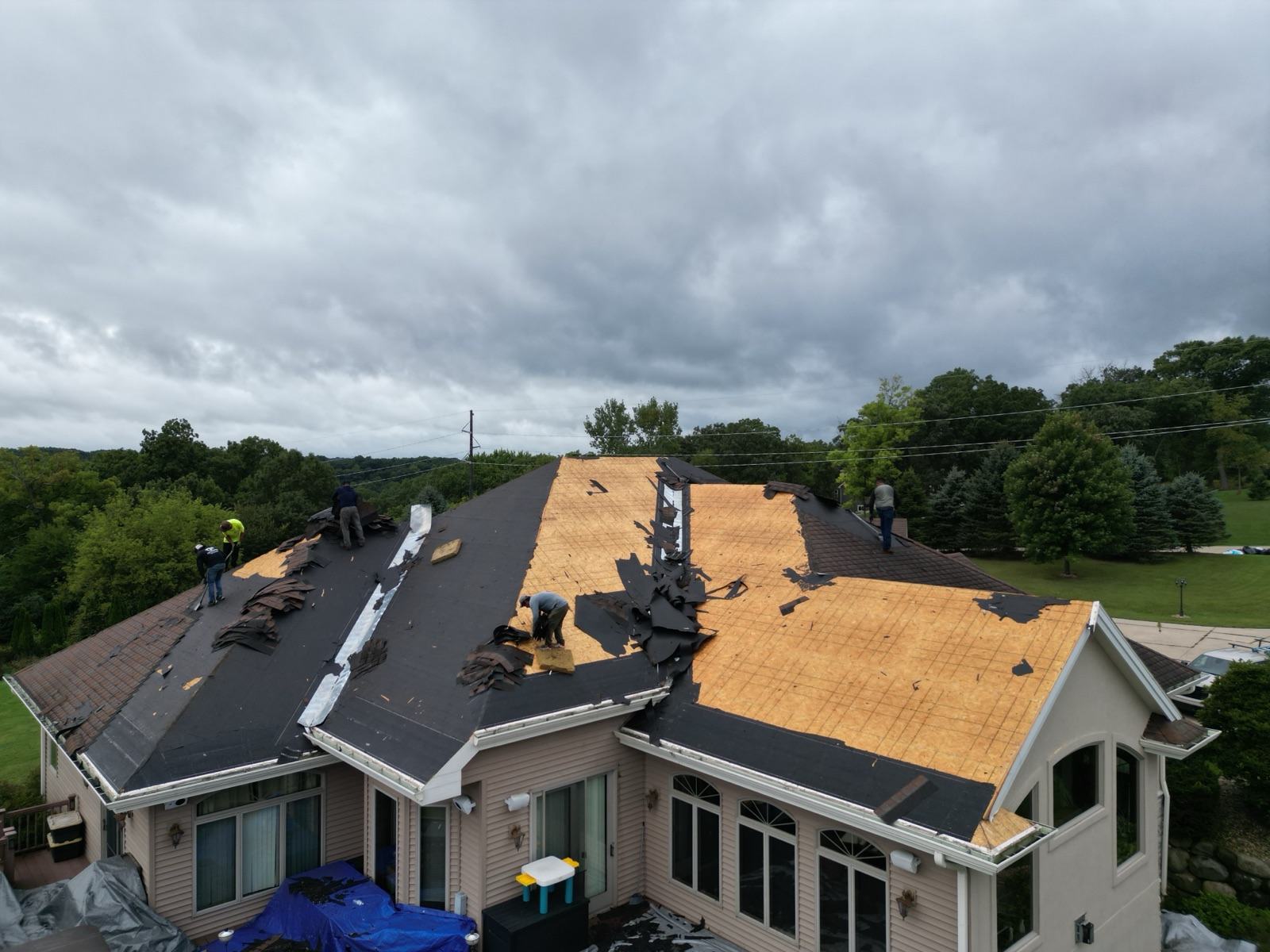 Drone view: crew tearing old shingles off a large ranch home under storm clouds