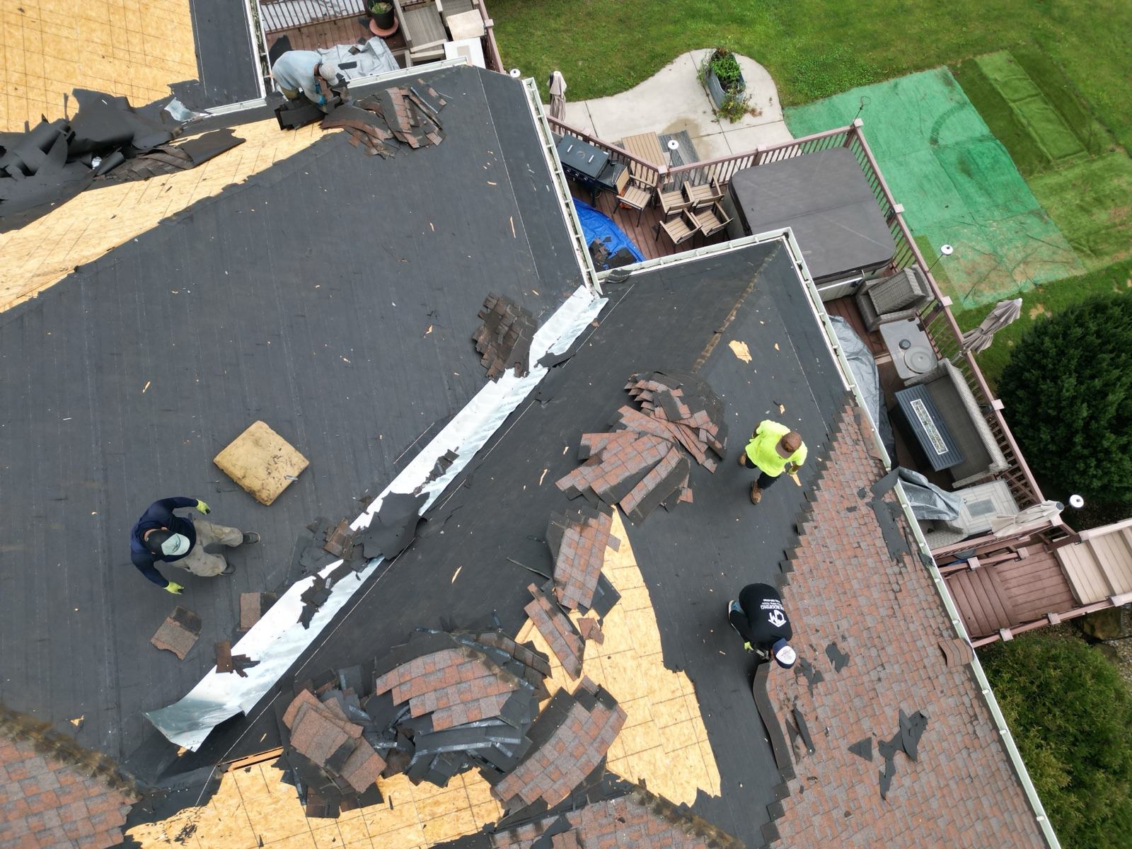 Top-down drone view: crew stripping shingles down to the underlayment