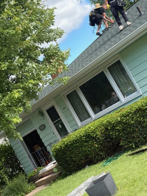 Two crew members on the roof of a mint-green house sizing up a fascia job